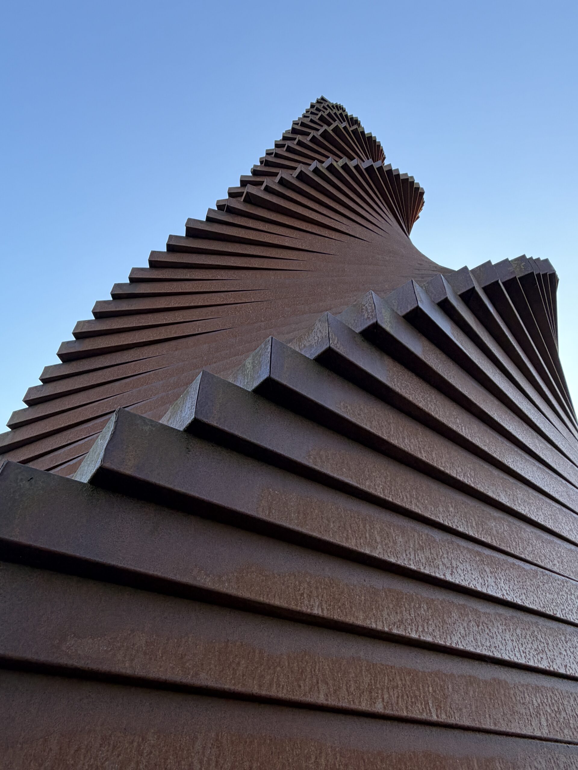 Schraubenförmige rostbraune Metallskulptur vor blauem Himmel