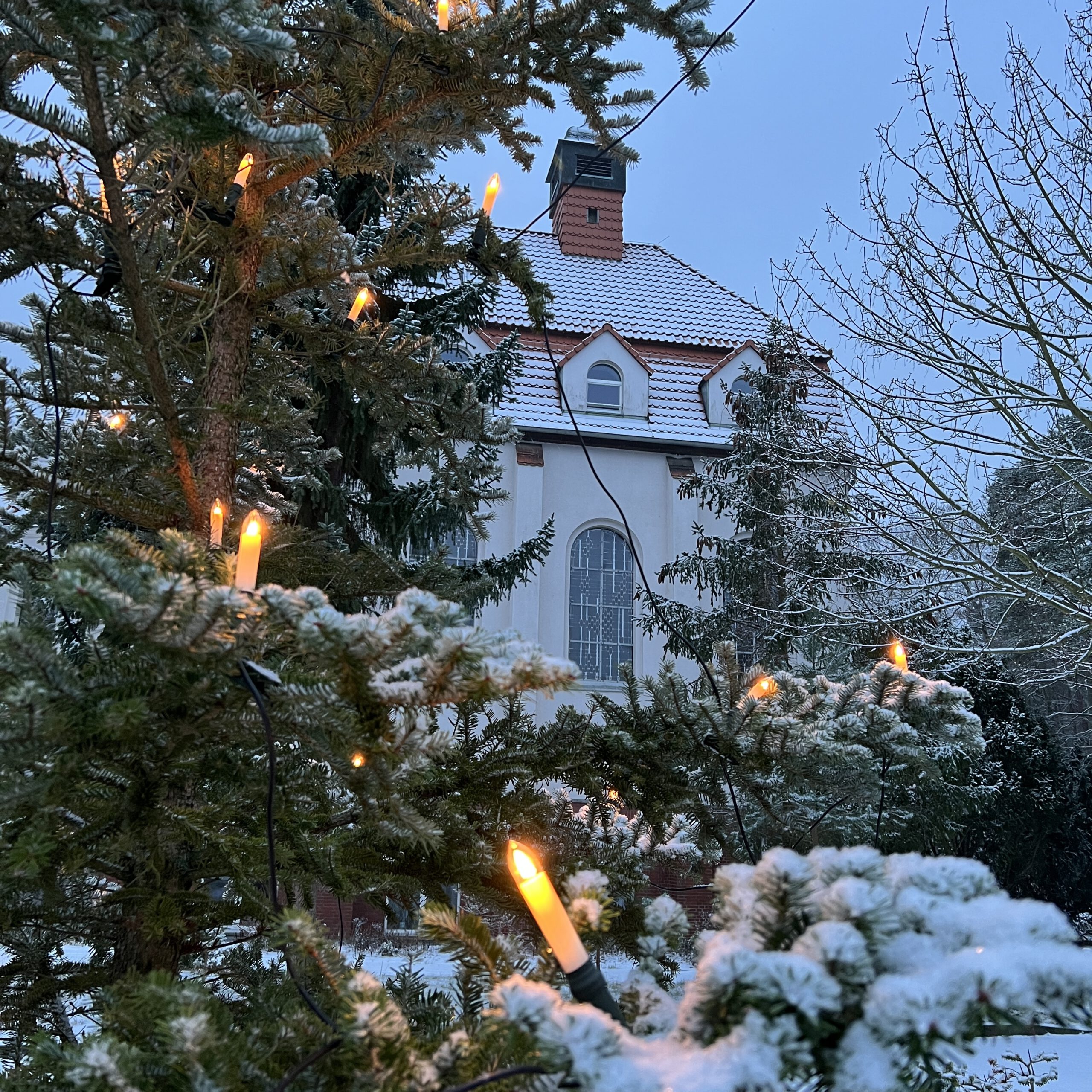 Das Haus St. Otto im winterlichen Schnee in der Abenddämmerung, im Vordergrund beleuchtete Tannenzweige