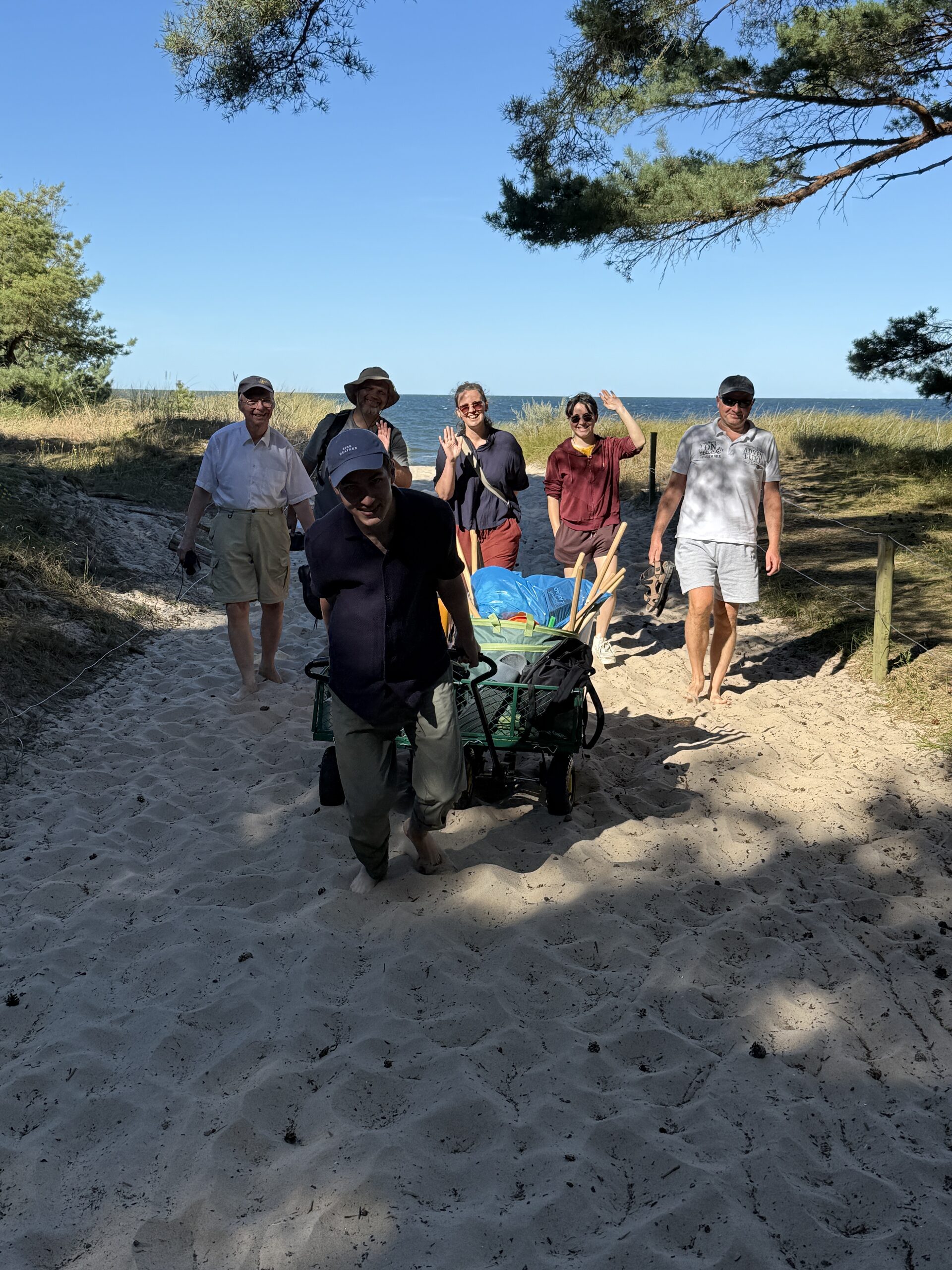 Gruppe mit Bollerwagen auf einem sandigen Weg durch die Dünen